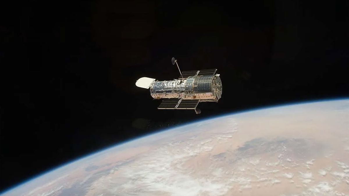 A metallic-wrapped spacecraft in space, which looks black, above Earth.